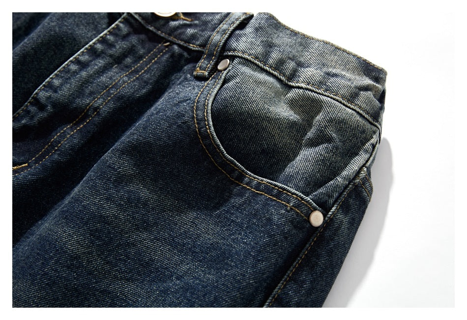 Close-up of a front pocket on dark washed jeans, with a metal rivet and contrasting stitching.