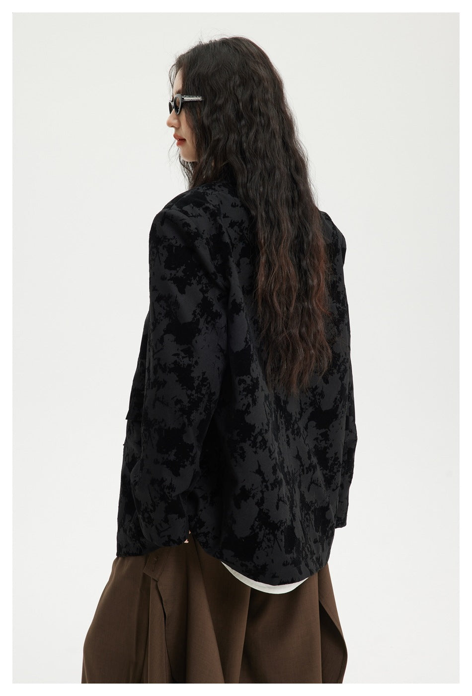 Rear three-quarter view of a model wearing a black abstract-patterned jacket, showing its long back and rounded hem.