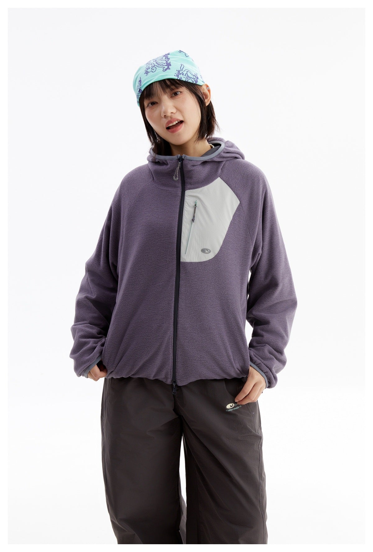 Waist-up view of a model wearing a purple hooded zip jacket with a pale asymmetrical zip pocket.
