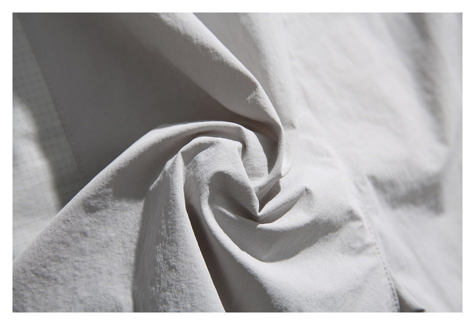 Close-up of pale gray garment fabric gathered into folds, with a small section of subtle grid-patterned fabric visible.