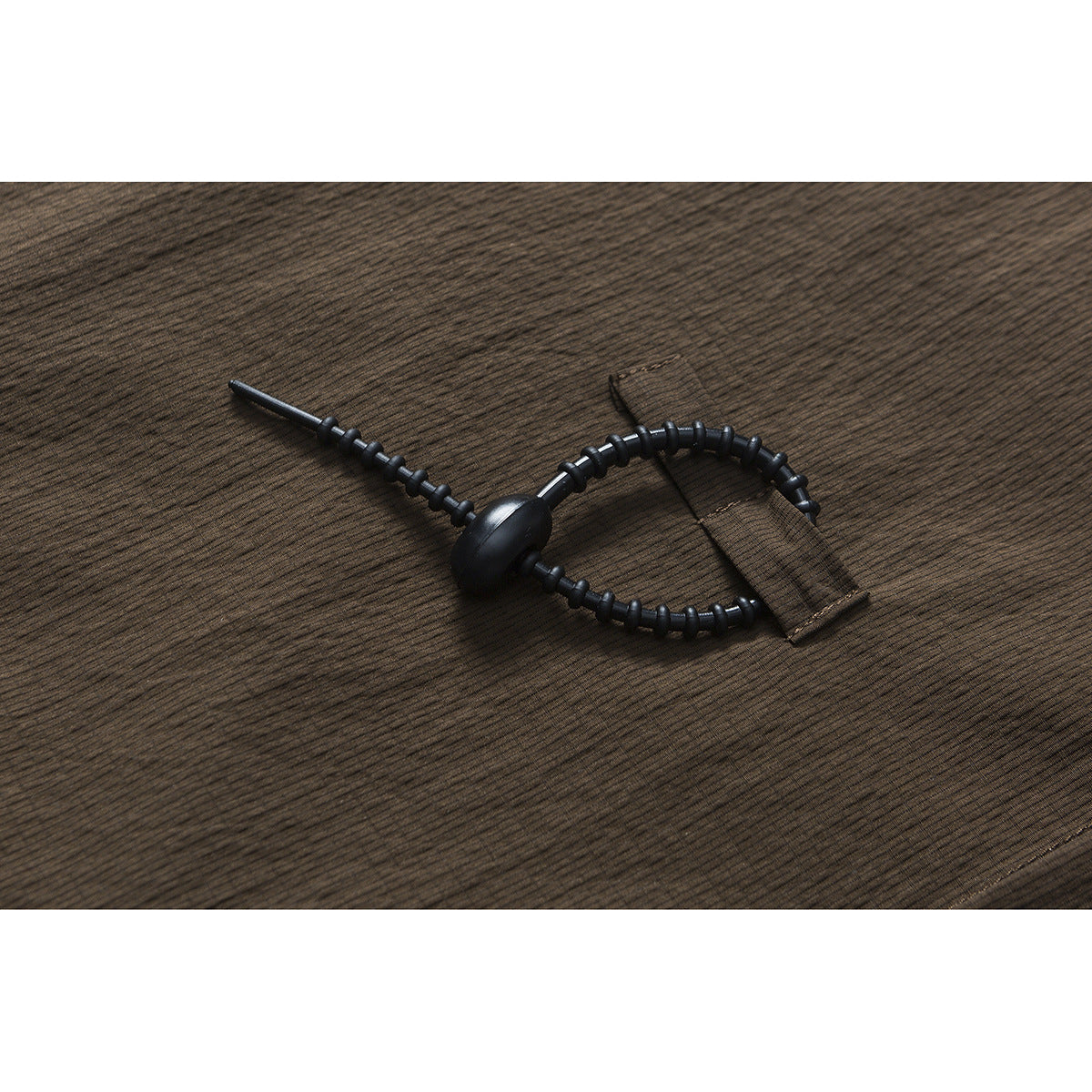 Close-up of a black adjustable cord toggle attached to dark brown striped fabric.