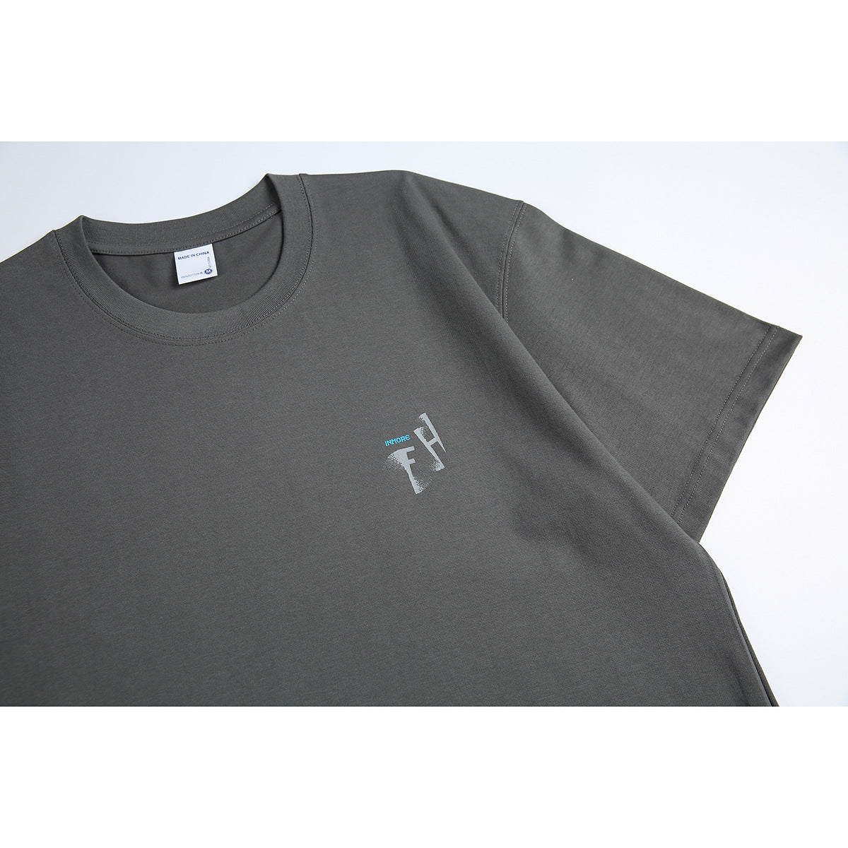 Close-up of a charcoal gray T-shirt showing its crew neck, short sleeve, and small chest graphic.
