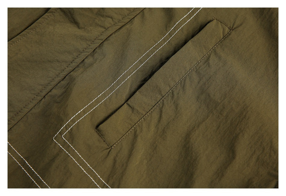Close-up of an olive jacket pocket flap with parallel contrasting stitch lines.