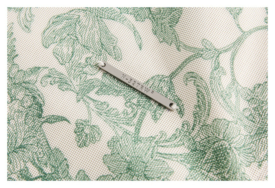 Close-up of green floral-patterned cream fabric with a small metal brand plate.