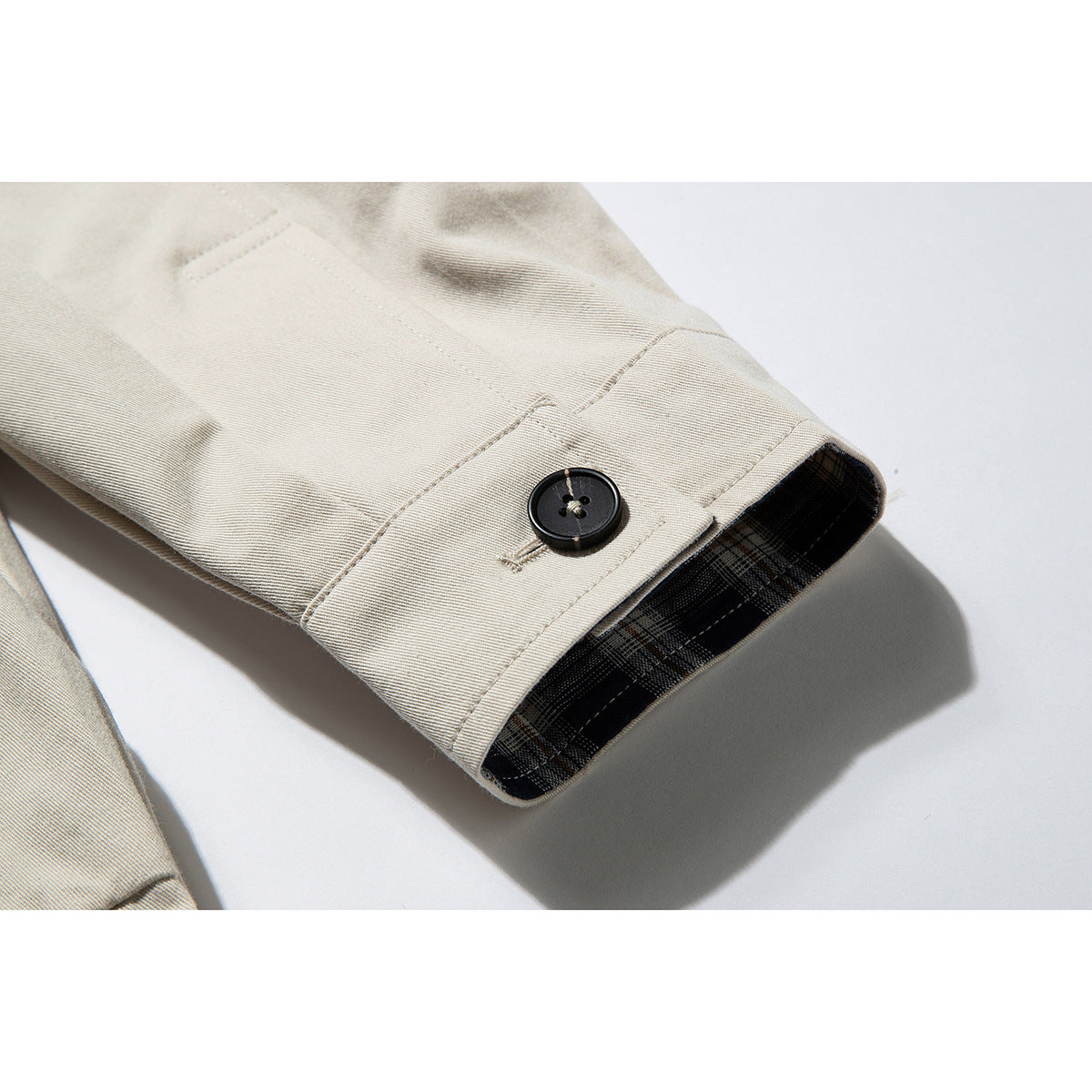 Close-up of a beige jacket cuff with a black button and dark plaid lining.