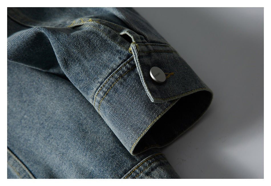 Close-up of a blue denim jacket cuff with yellow stitching and a metal button.