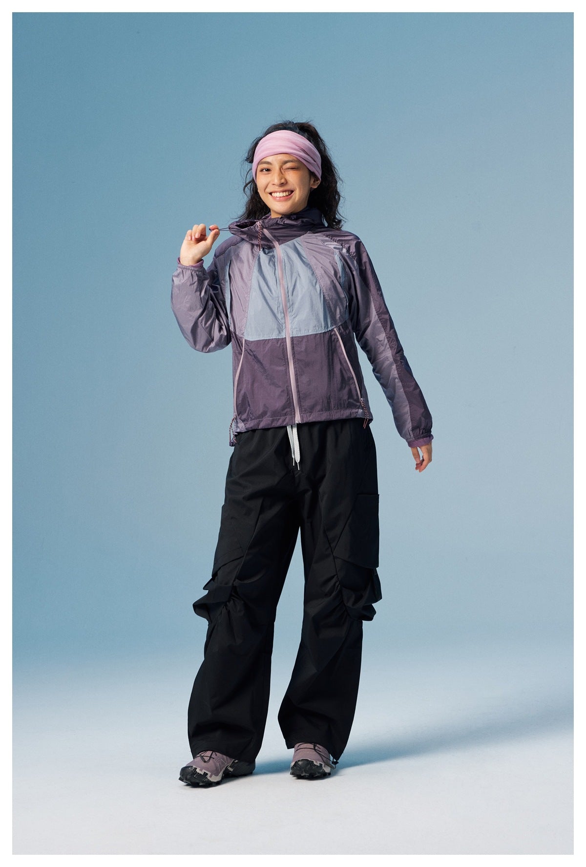 Model wearing a purple and pale blue color-block hooded jacket with black cargo pants, shown full length from the front.