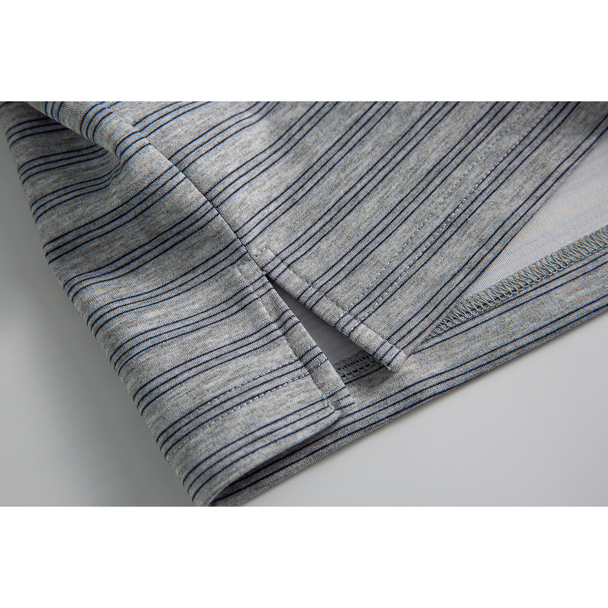 Close-up of the hem and stitched seam on a light gray polo with fine dark stripes.