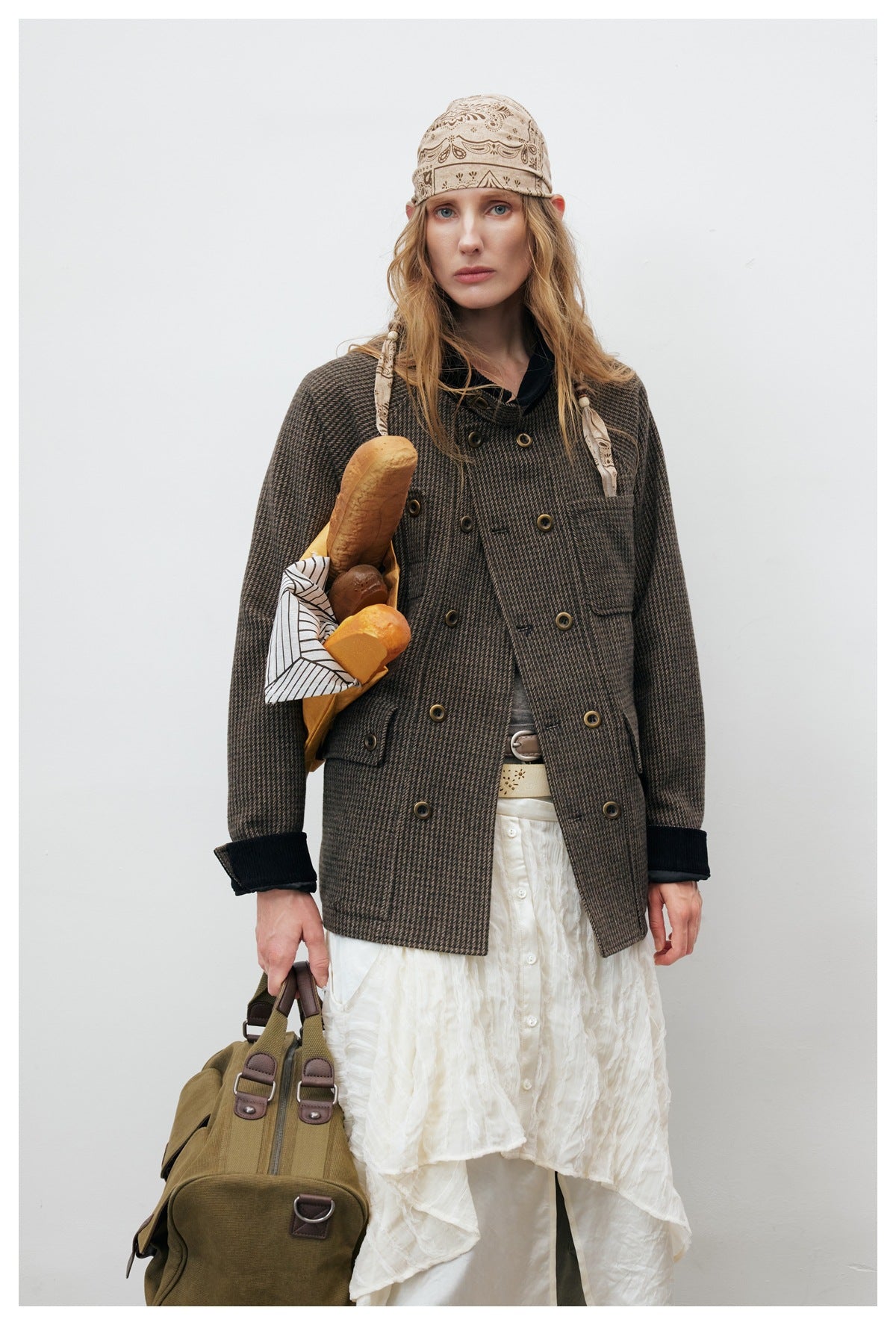 Model wearing the brown houndstooth double-breasted jacket open at the front over a white skirt, holding bread and a bag