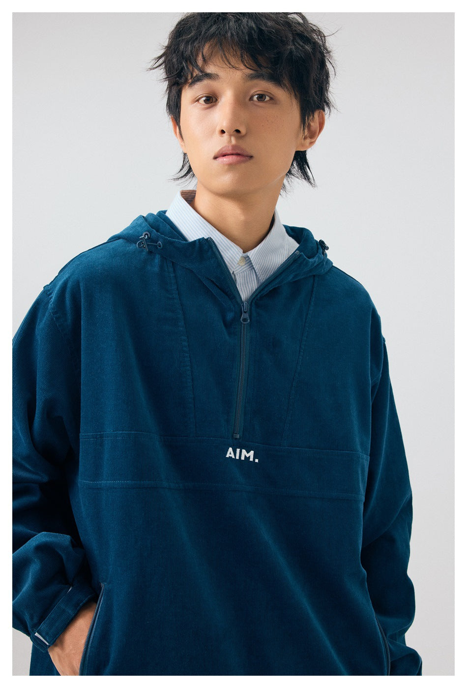 Close-up of a model wearing a navy hooded pullover with a short zip and white AIM chest print.