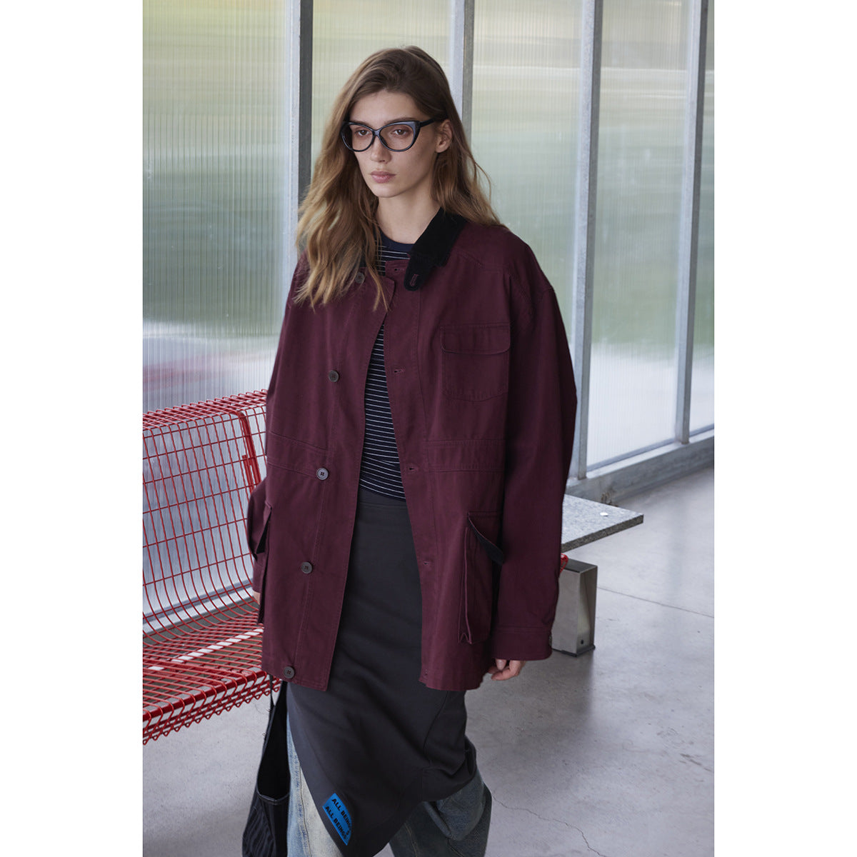 Model wearing a burgundy button-front utility jacket with a black collar and multiple pockets.