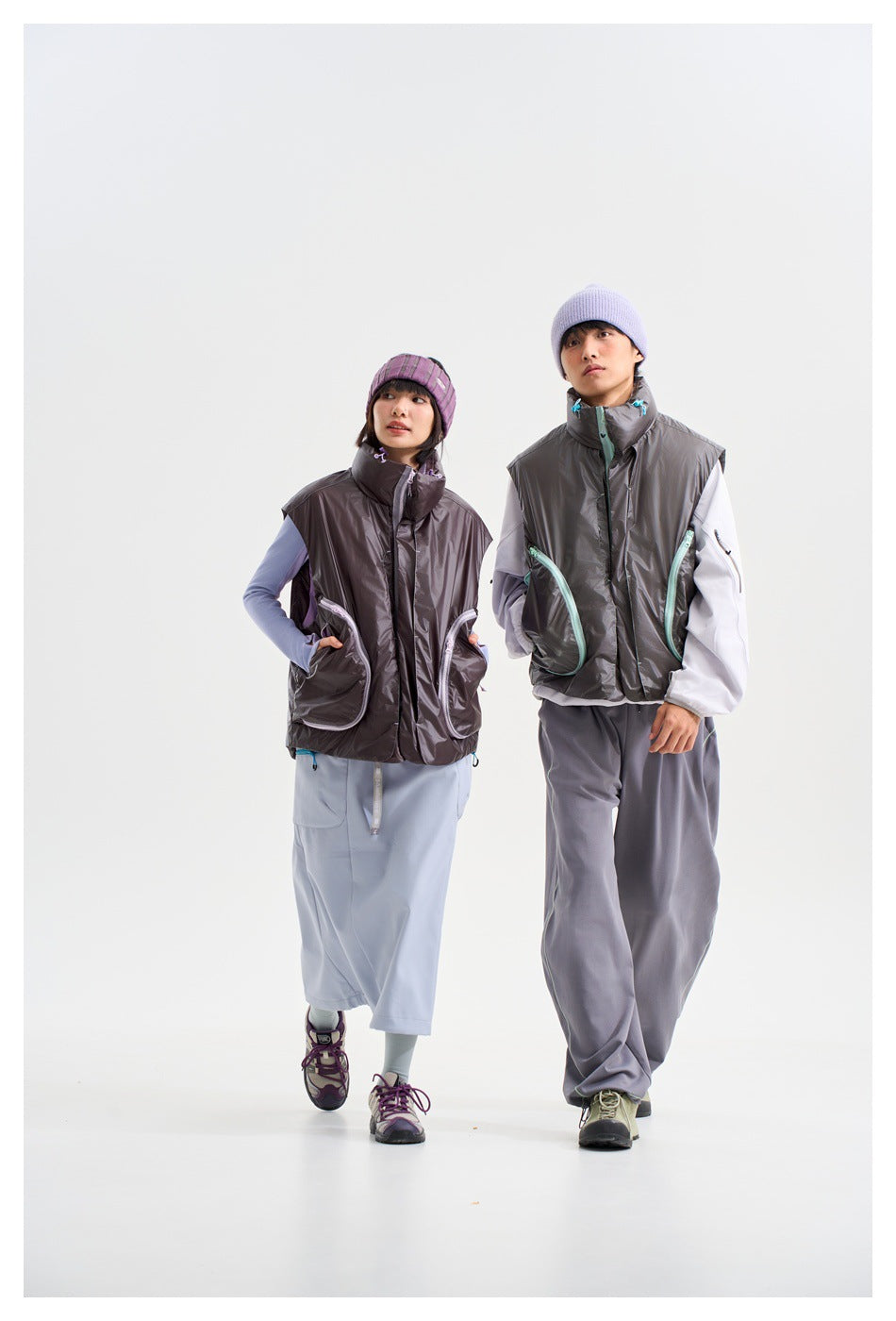 Two models wearing charcoal sleeveless vests with contrast pocket trim, styled with a pale blue skirt or gray trousers.