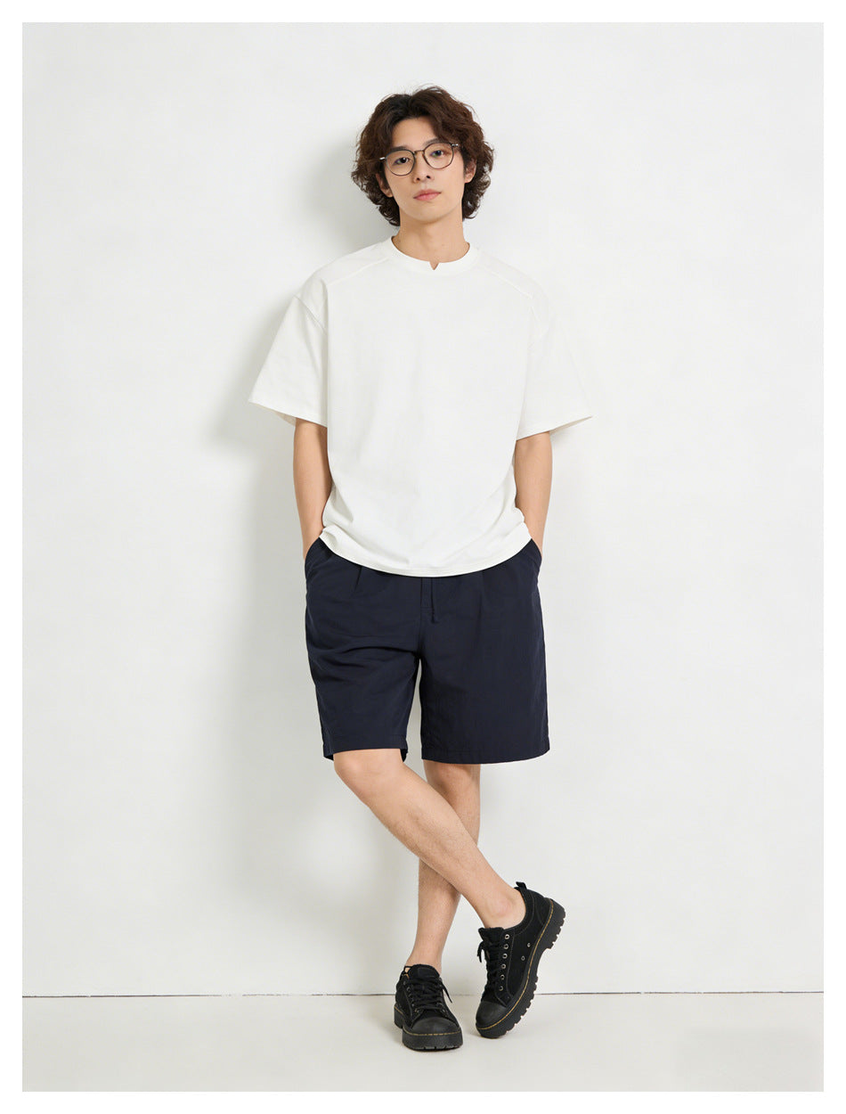 Model wearing a white short-sleeve T-shirt with navy shorts and black shoes against a light background
