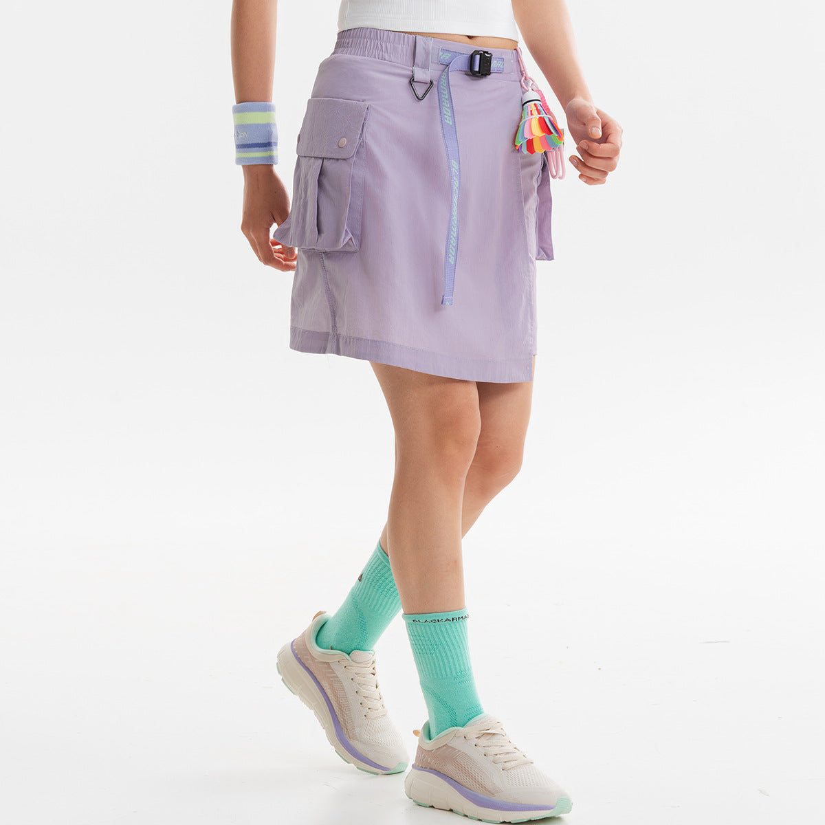 Model wearing a lavender wrap-style utility skirt with a belt, long hanging strap and flap cargo pockets.