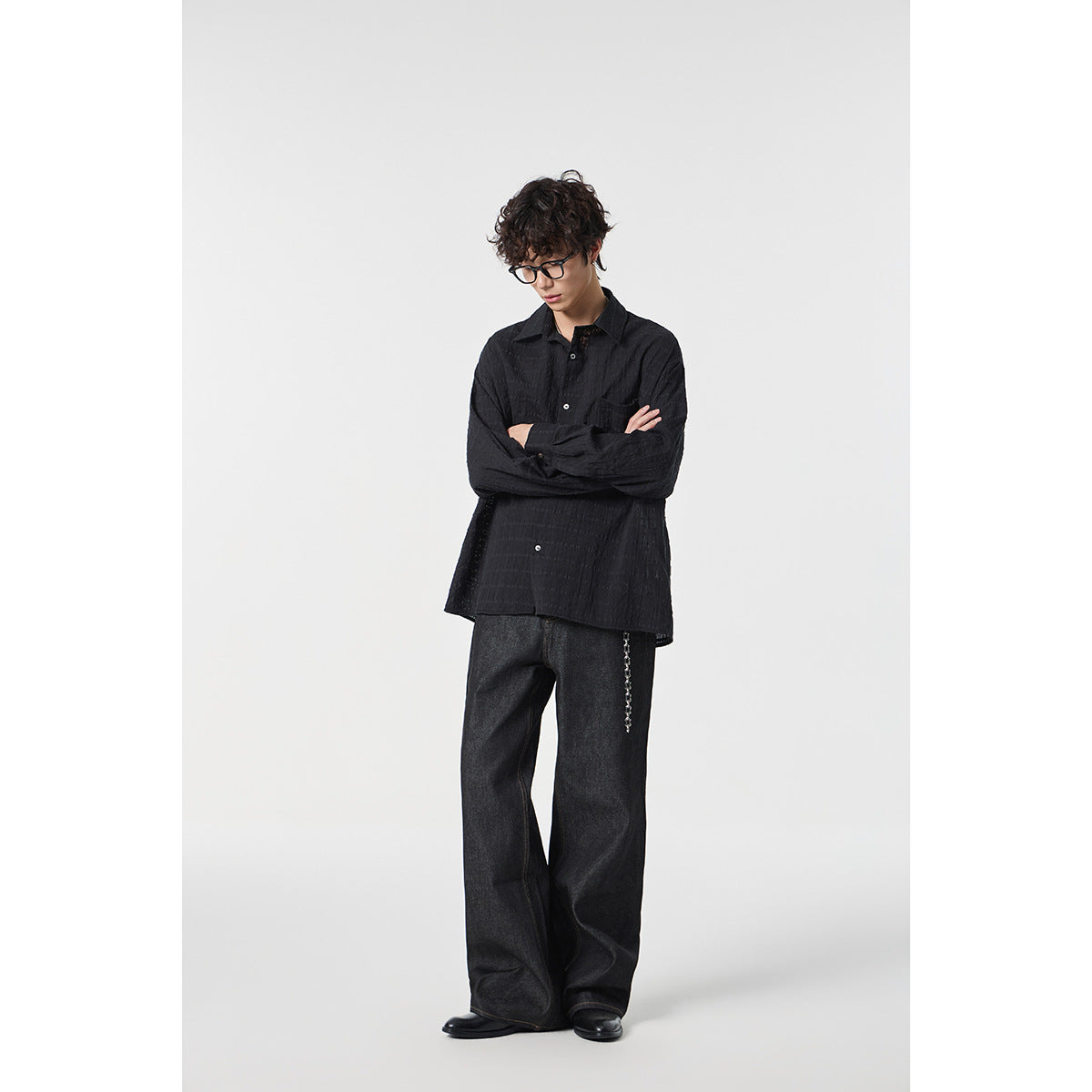 Full-length model wearing a black textured button-up shirt, dark wide-leg jeans, and black shoes.