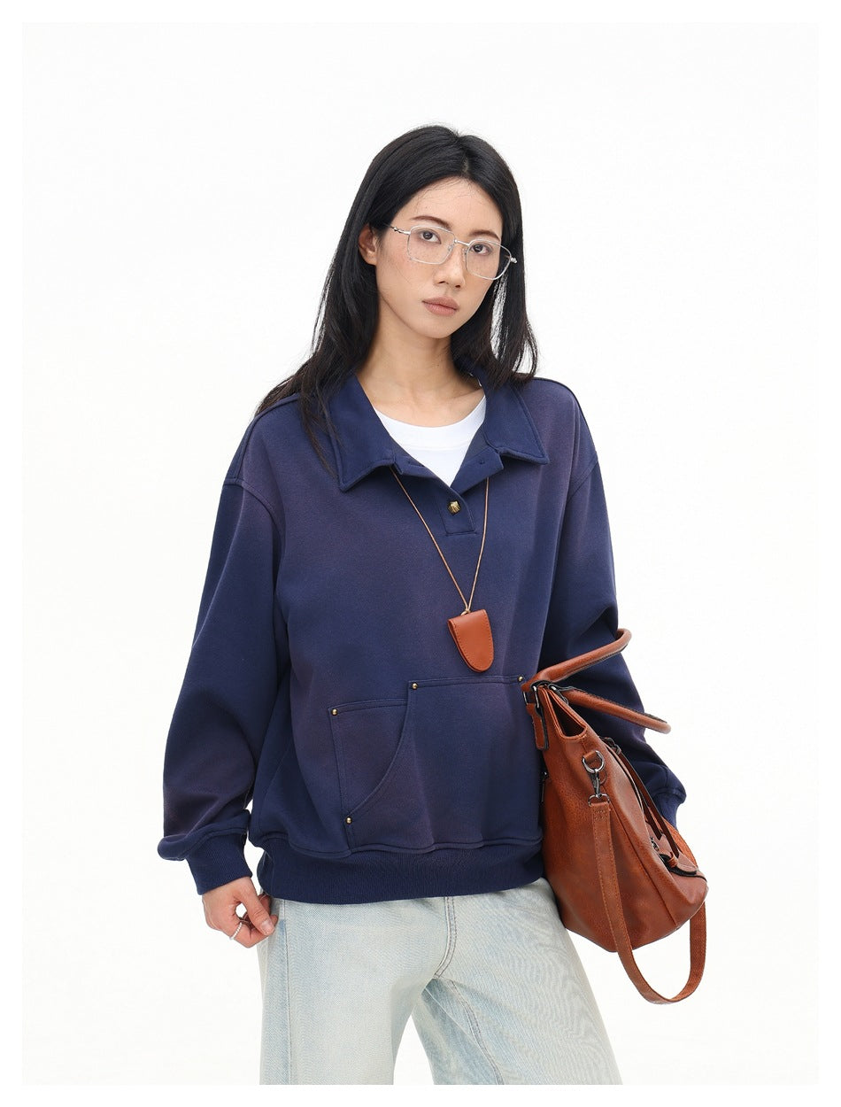 Model in a navy collared pullover with a pouch pocket and pale jeans, carrying a brown handbag.