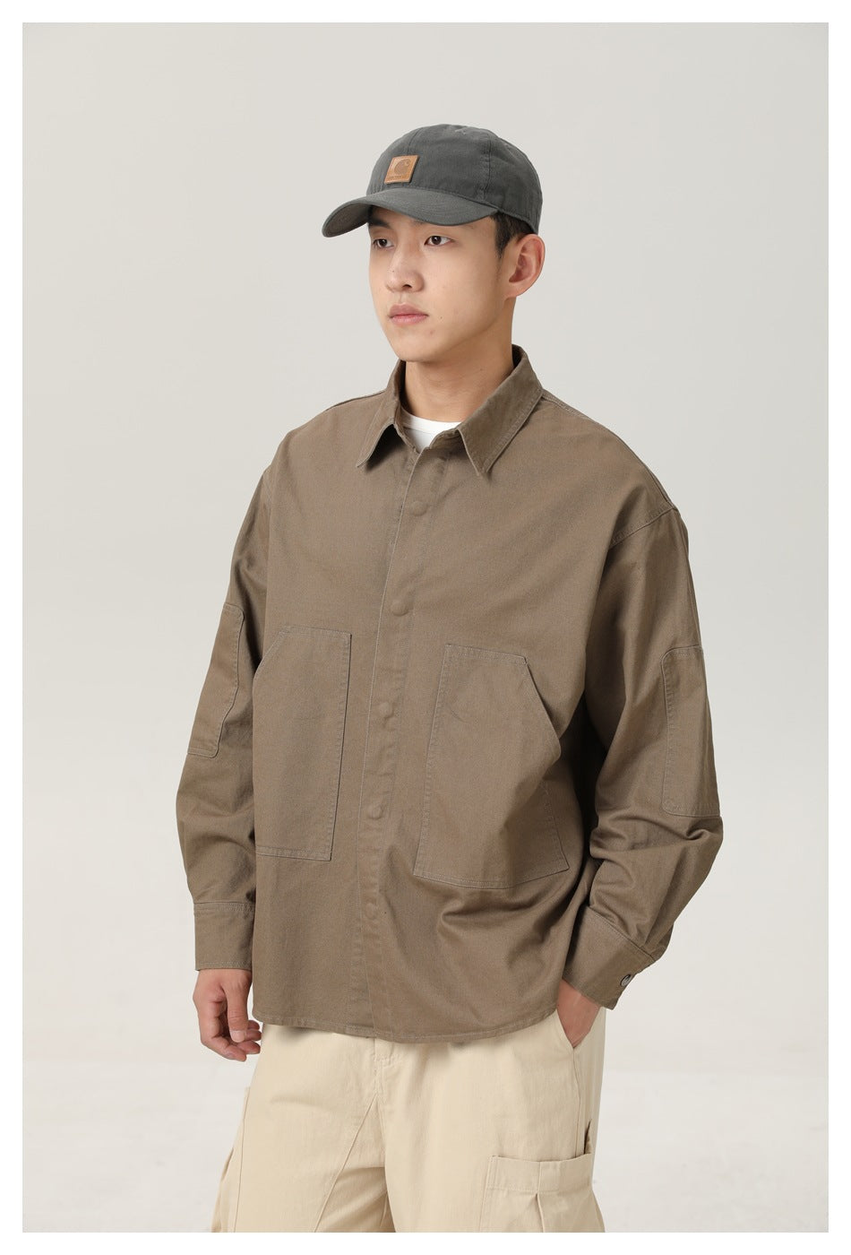 Model wearing a brown overshirt with two large front pockets and sleeve pockets, paired with cream pants.