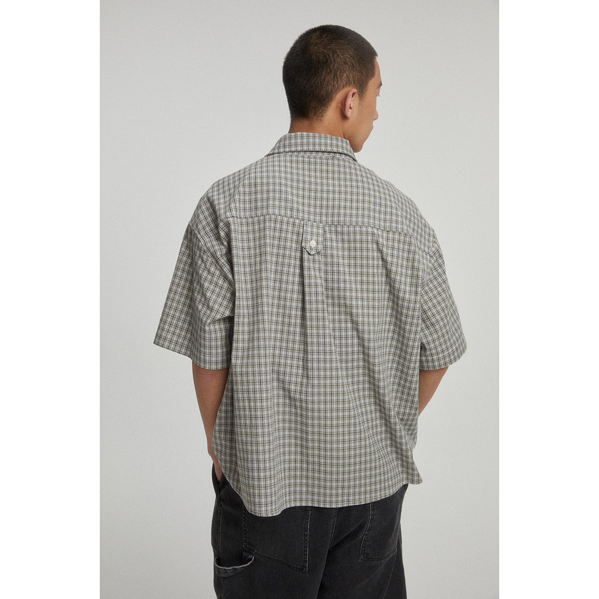 Back view of a model wearing a gray checked short-sleeve shirt and dark shorts.