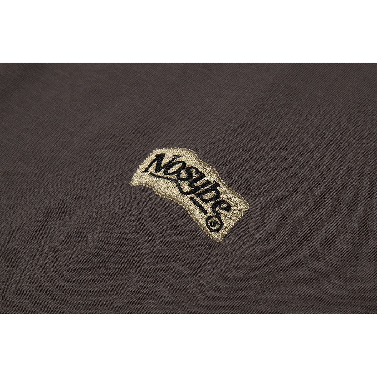 Close-up of a small gold embroidered wordmark on dark brown shirt fabric.
