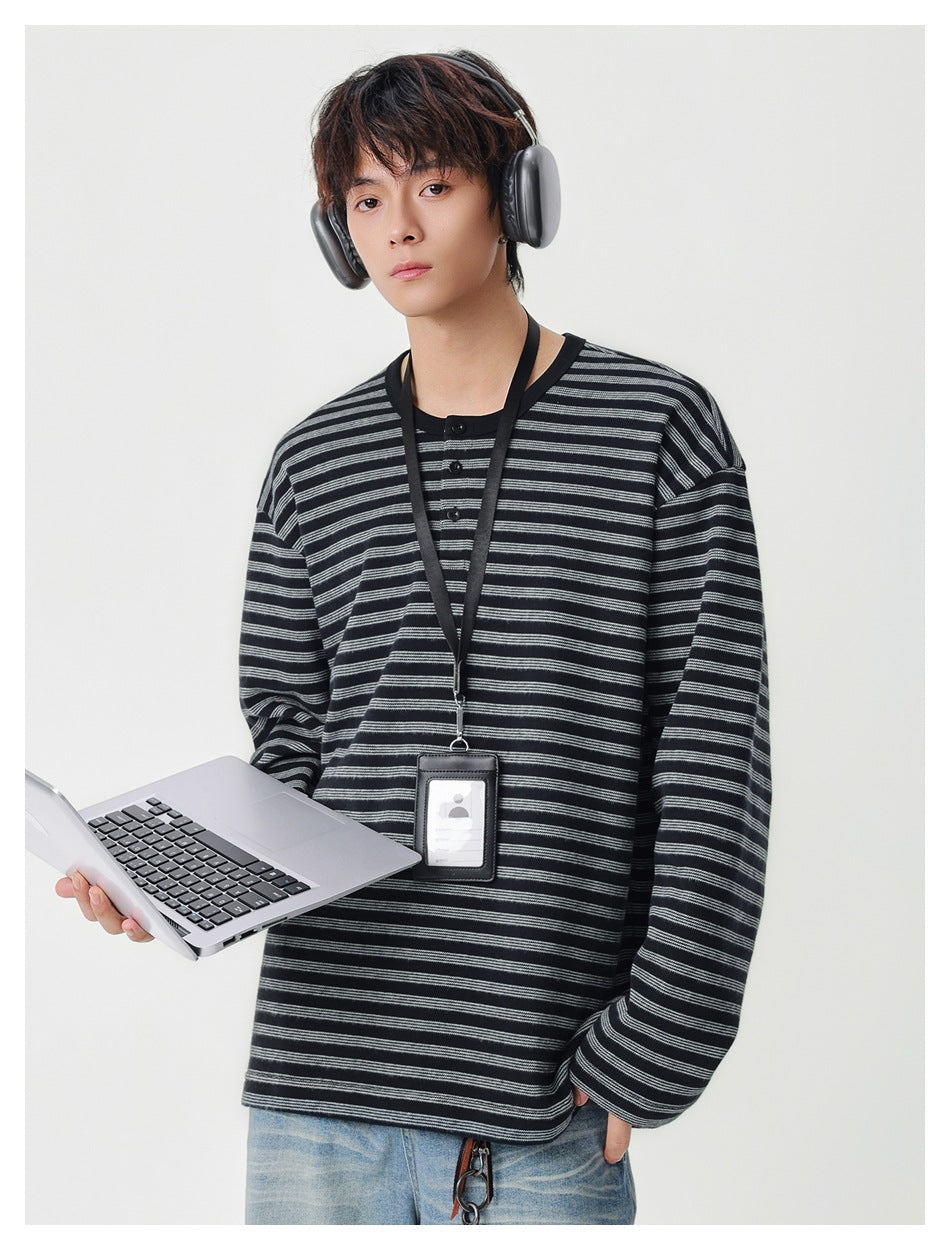 Model wearing a loose black and gray striped long-sleeve henley with a short button placket.