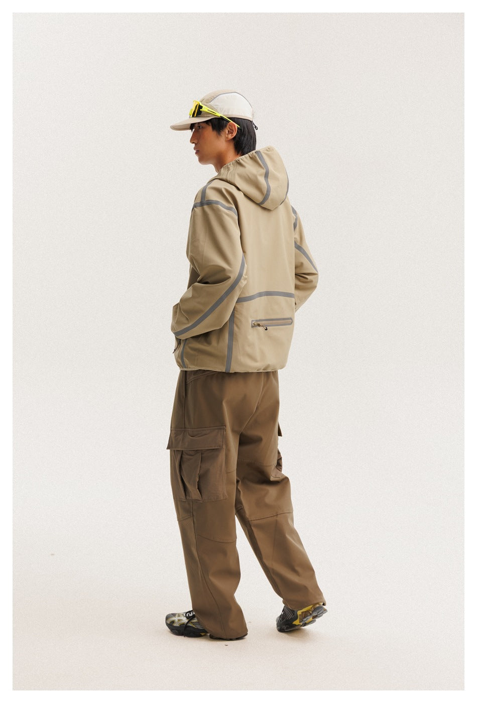 Three-quarter rear view of a model wearing a tan hooded jacket with gray accents and brown cargo pants.