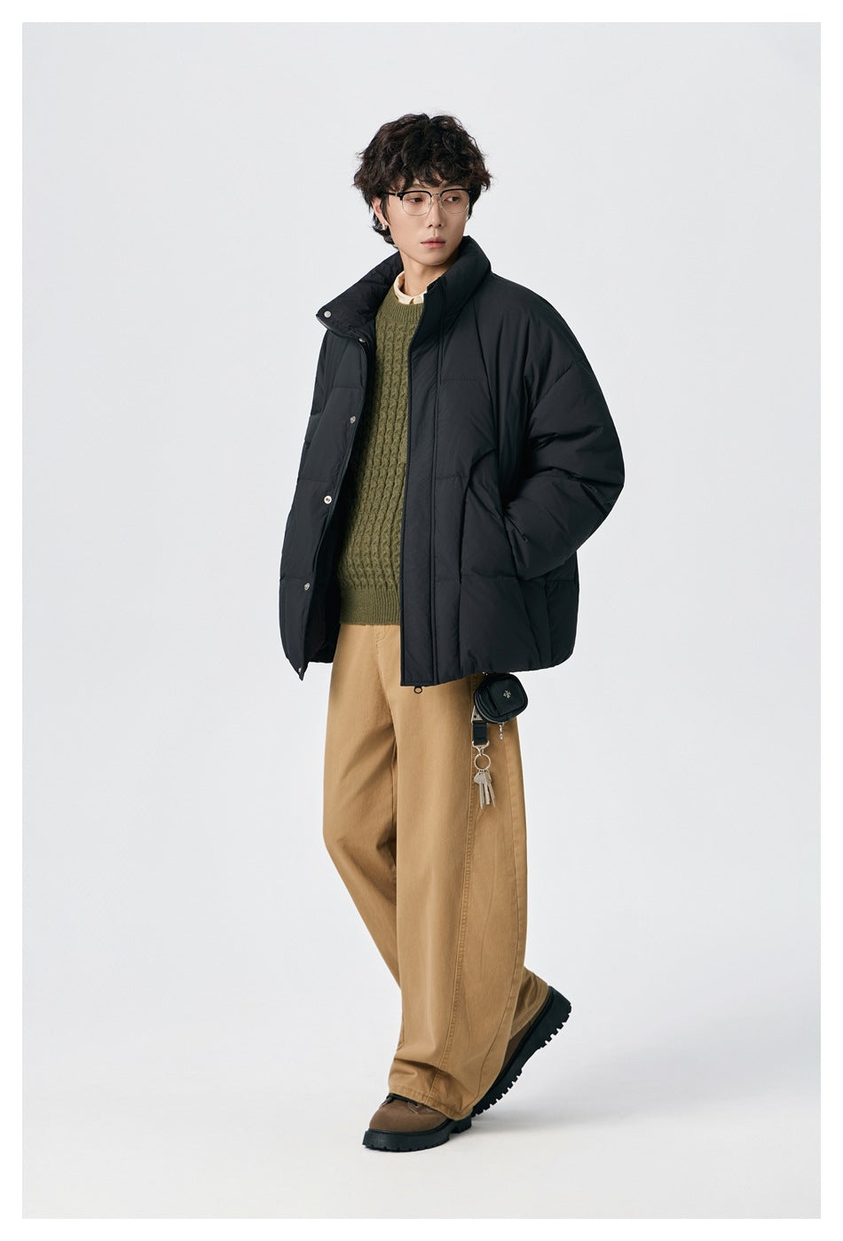 Model wearing an open black puffer jacket over an olive sweater, shown from the front.
