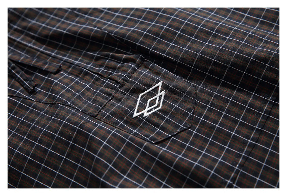 Close-up of a flap pocket and white geometric emblem on dark plaid fabric.