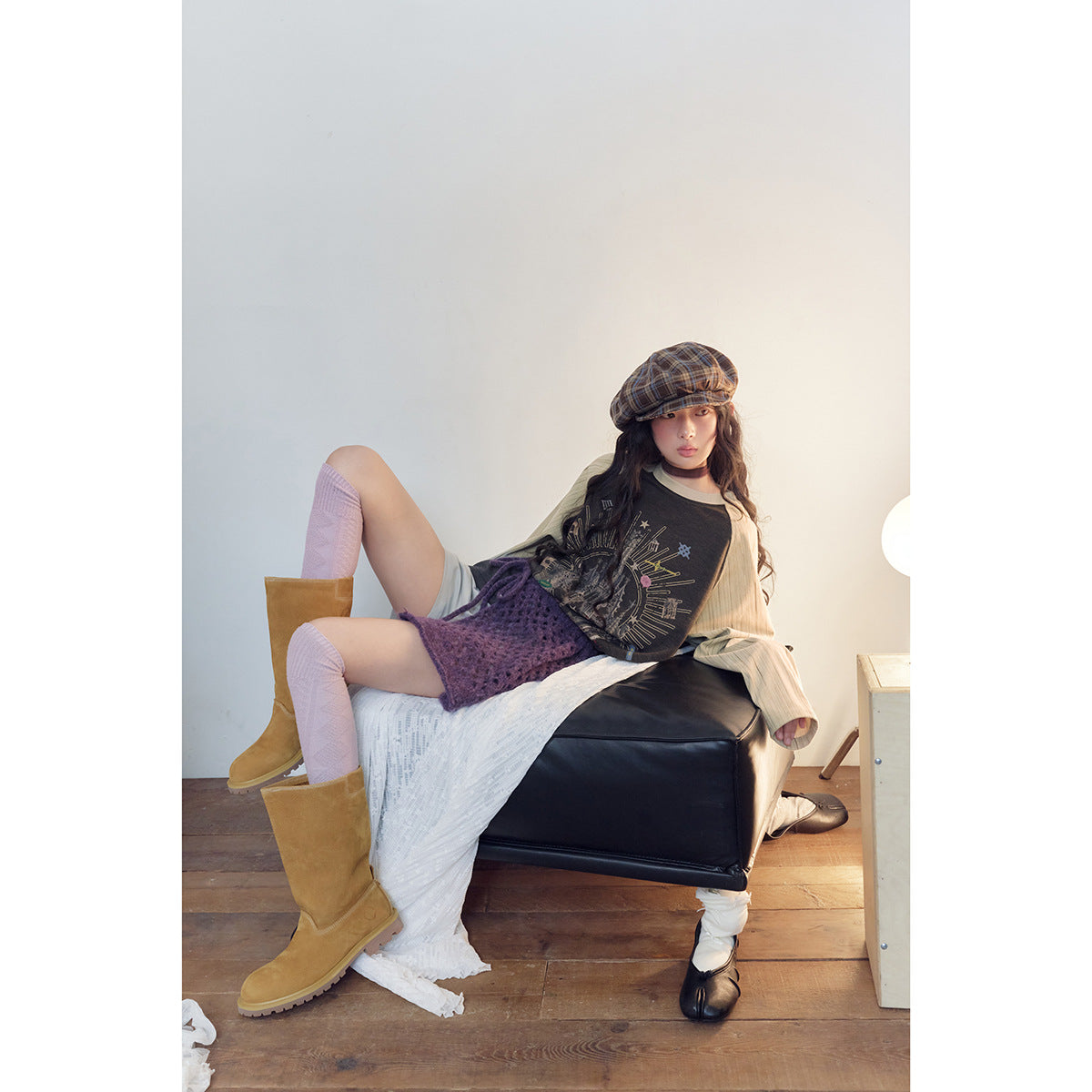 Model seated wearing a charcoal graphic raglan top with cream striped sleeves and a purple knit wrap skirt.