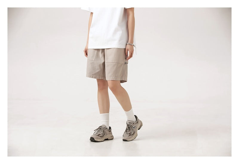 Cropped angled front view of a model wearing light beige shorts with front pockets.