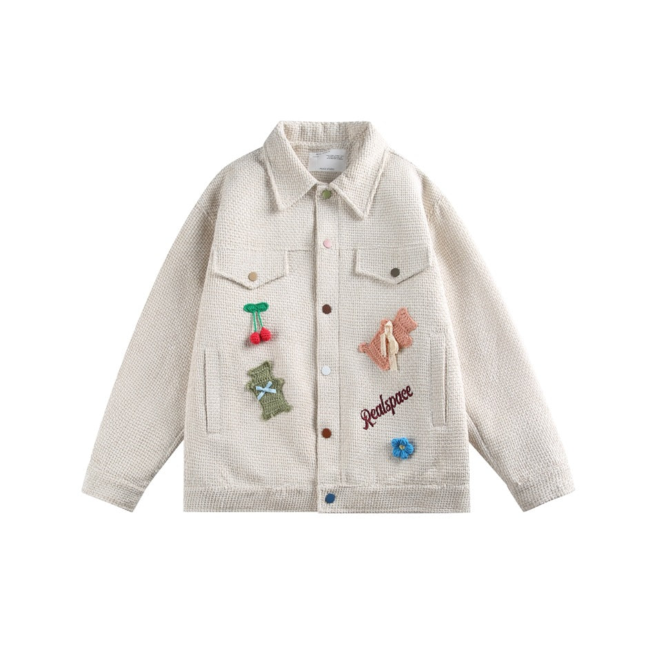 Light khaki textured jacket, front flat lay, with colorful snap buttons, flap pockets and crochet cherry, bear and flower