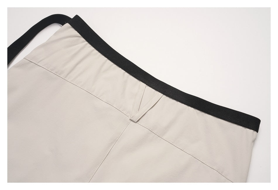 Close-up of light beige garment waistband with a black webbing belt and stitched seams.