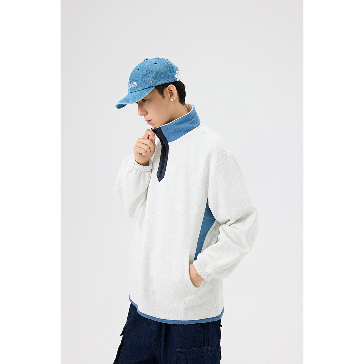Man wearing a light gray pullover with a blue stand collar and side panels, navy quarter zip, and kangaroo pocket.