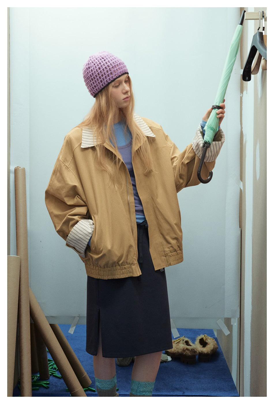 Model wearing a tan oversized jacket with striped collar and cuffs, shown at an angle.