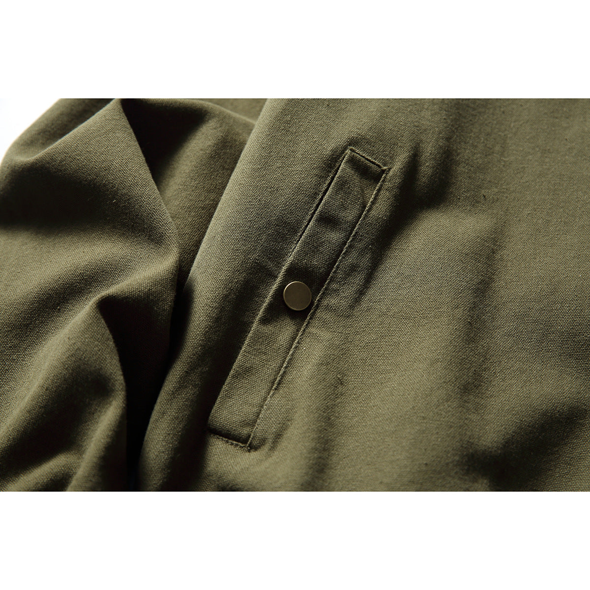 Close-up of an olive jacket's angled welt pocket with a round brass-tone snap.