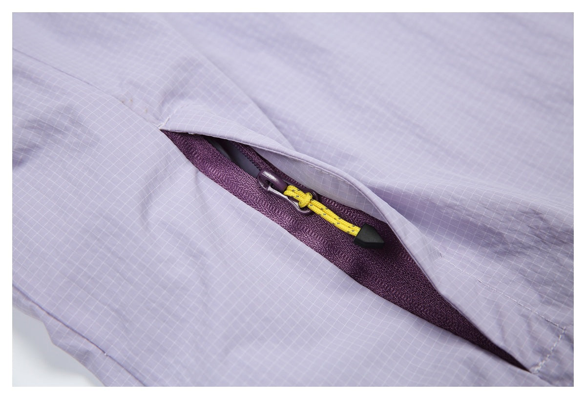 Close-up of a lavender grid-patterned garment's pocket, with a plum zipper and yellow-and-black pull beneath a flap.