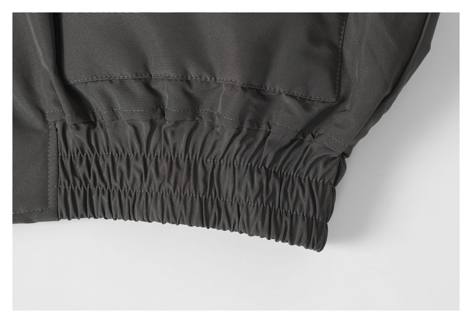Close-up of the charcoal jacket’s gathered elastic hem and lower flap pocket.