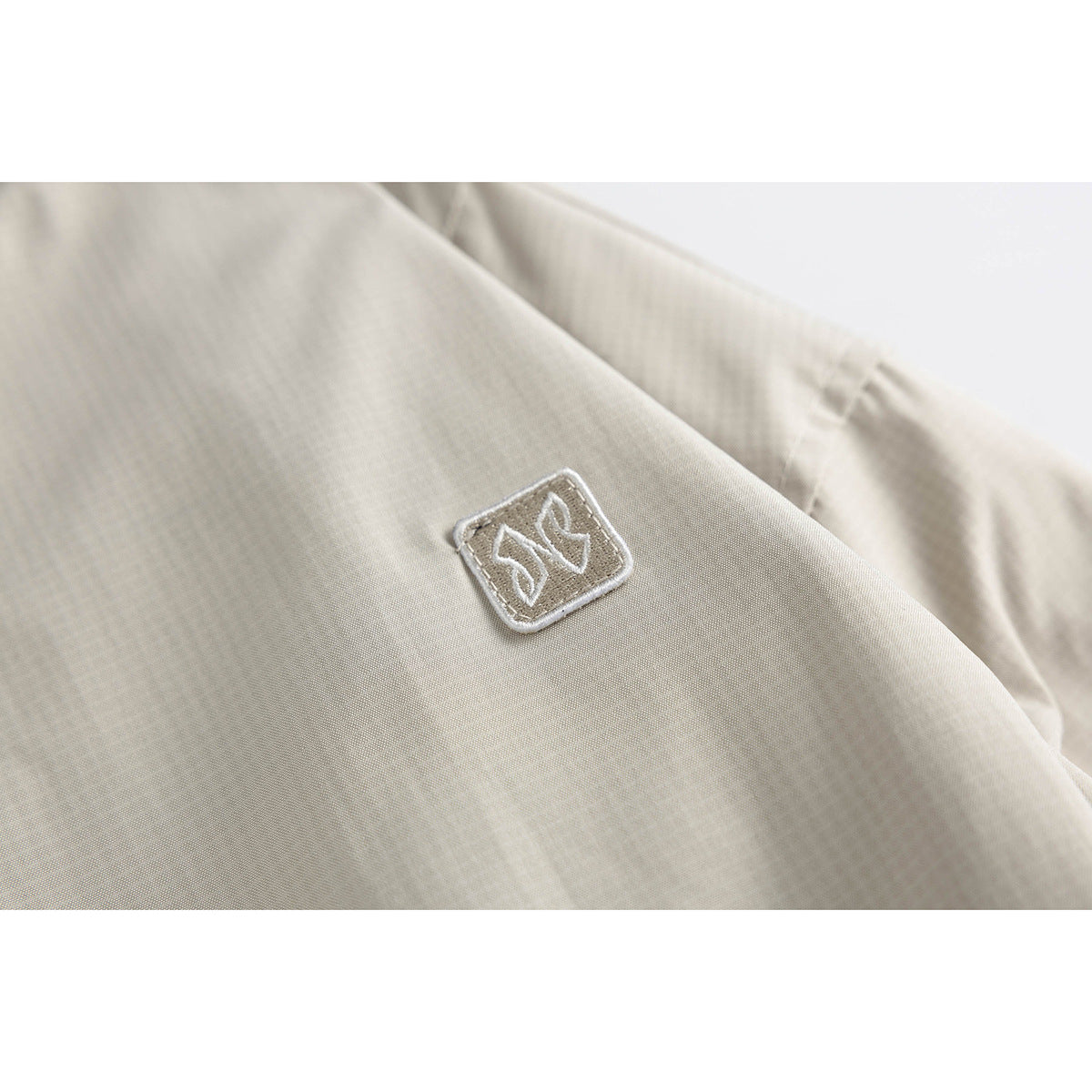 Close-up of a small square embroidered patch on the light beige jacket.
