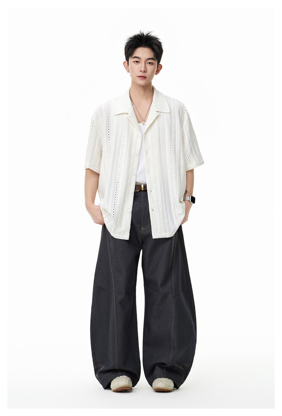 Full-length front view of a model in an ivory openwork short-sleeve shirt and wide-leg dark trousers.