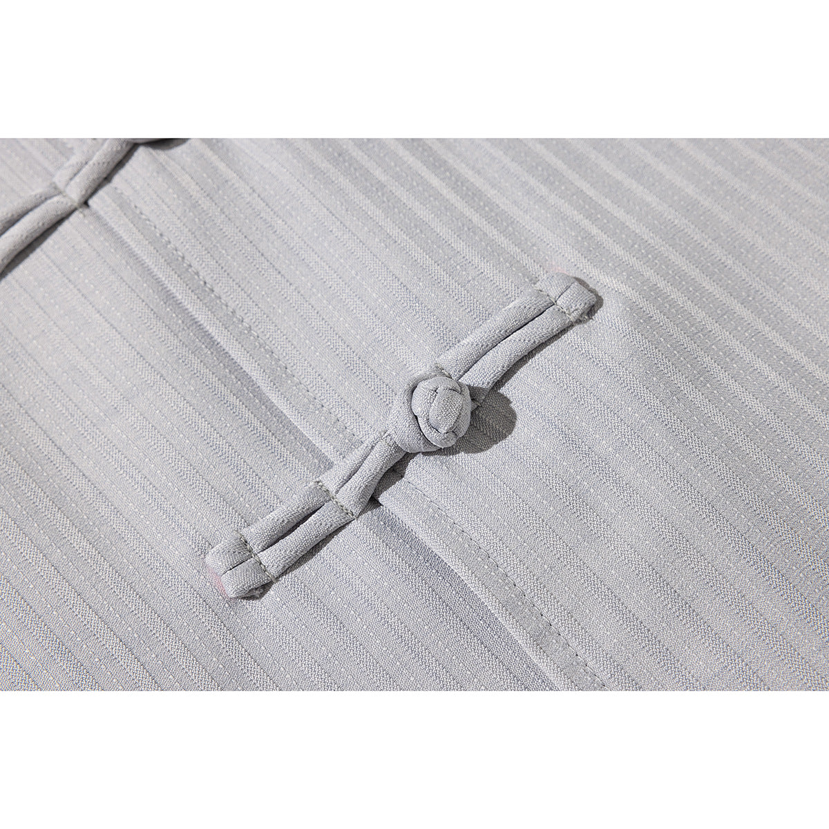 Close-up of a fabric frog closure and subtle vertical stripes on a light gray shirt.