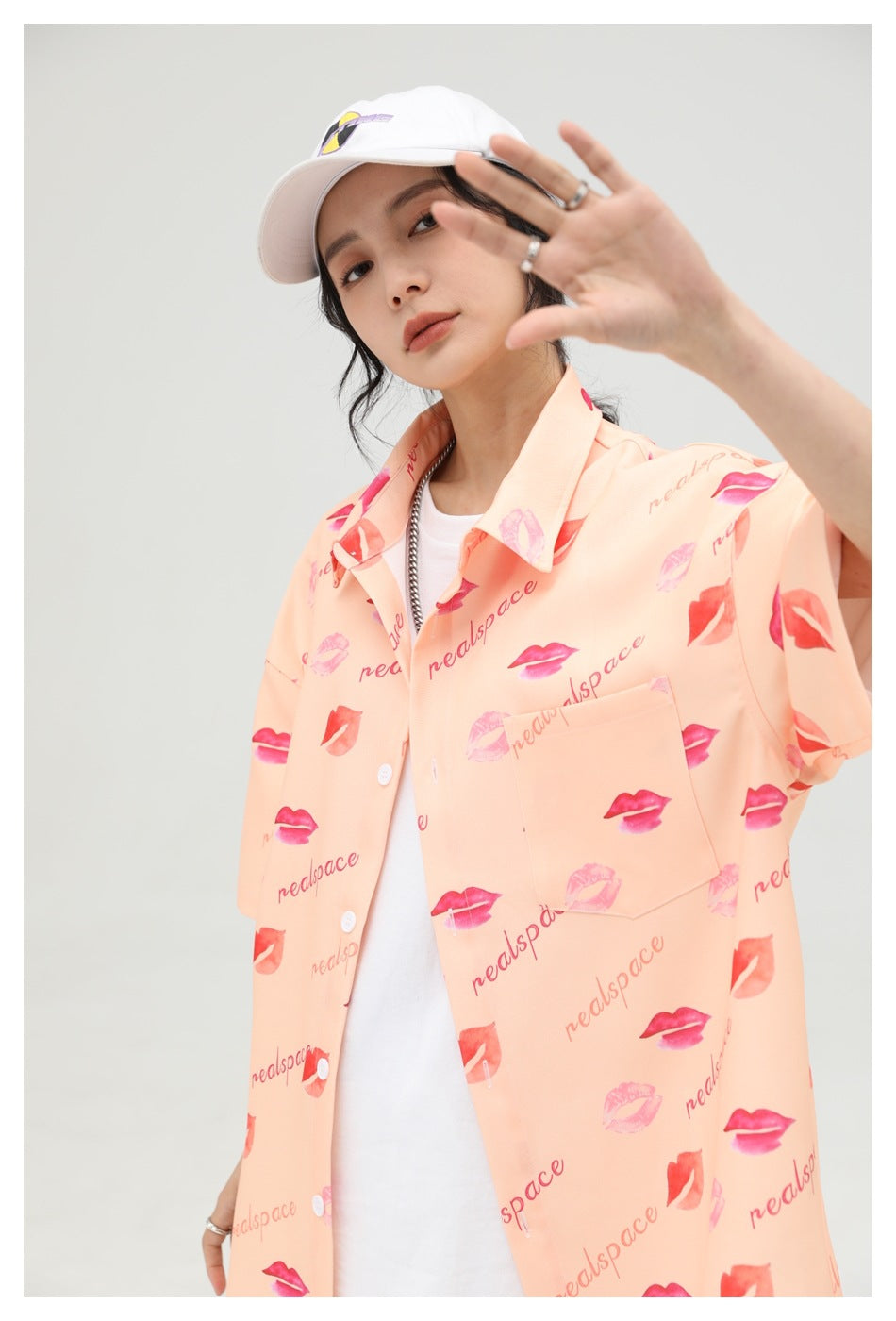 Model wearing the front of a peach short-sleeve button-up shirt with lipstick prints, lettering, and a chest pocket.