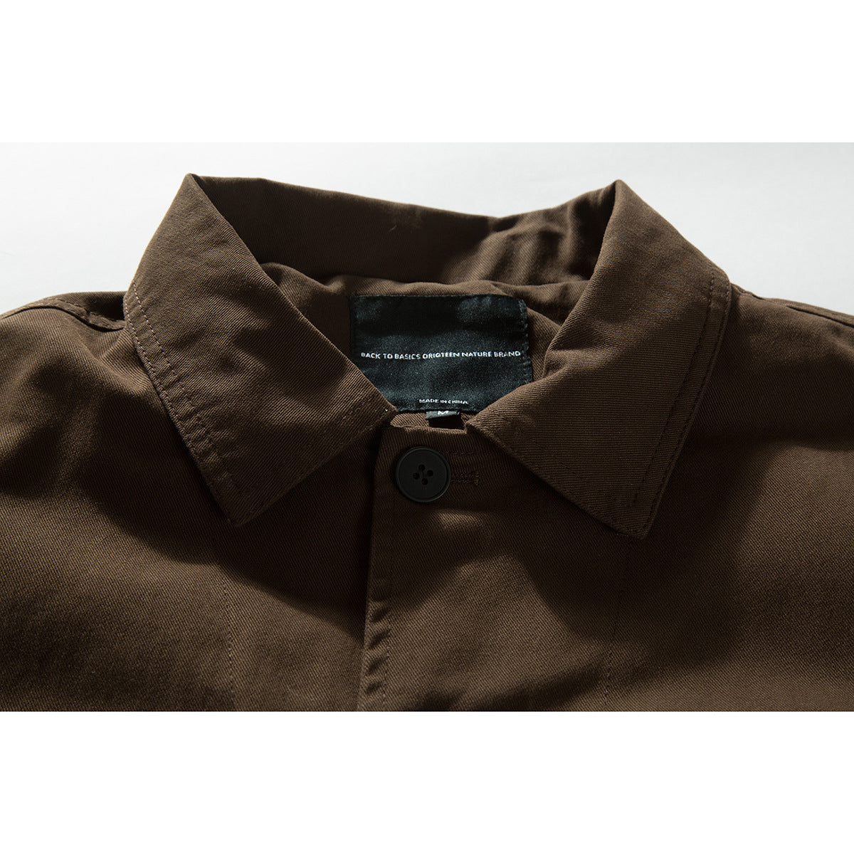 Close-up of a dark brown shirt collar, black button, and inner neck label.
