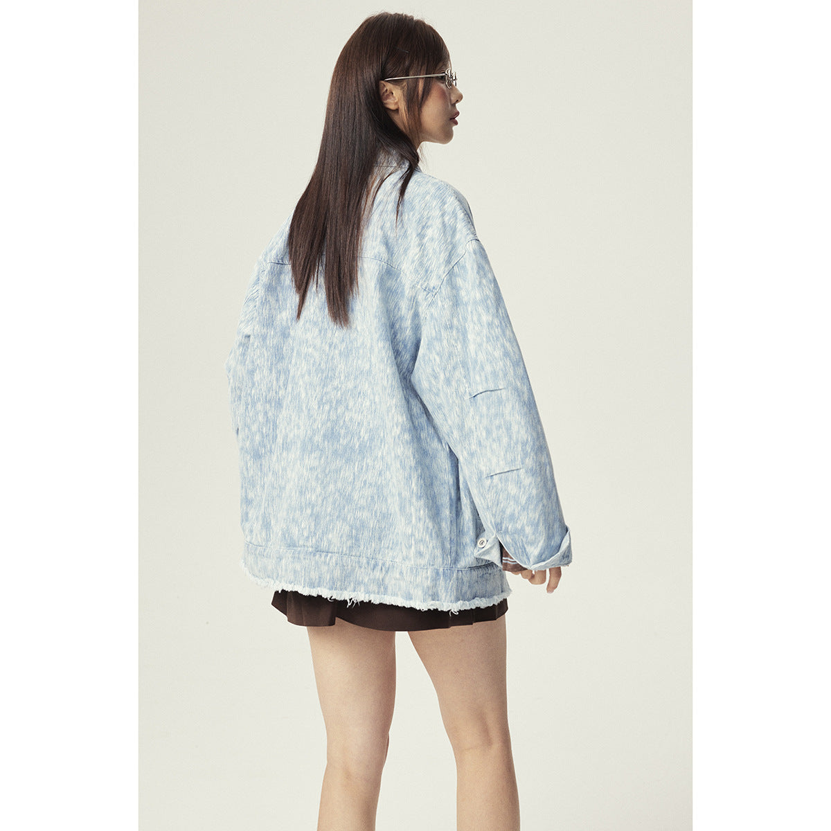 Side-back view of a model wearing an oversized pale blue mottled jacket with a frayed hem.