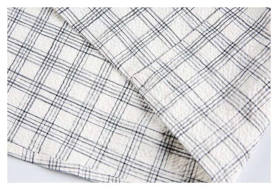 Close-up of off-white fabric with black and gray plaid, showing a folded edge and seam.