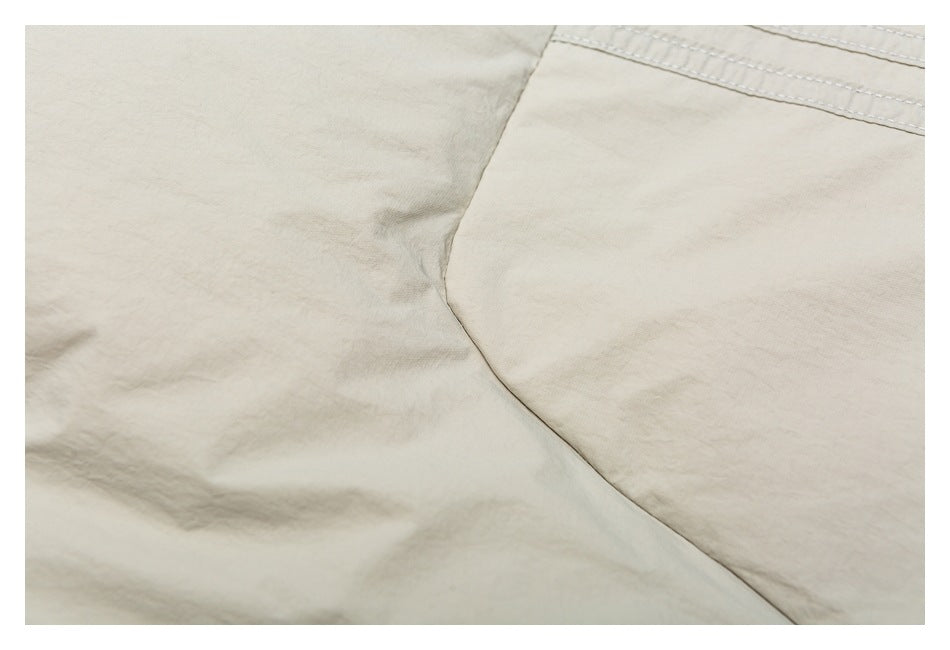 Close-up of a curved seam and stitched panel on light beige jacket fabric.