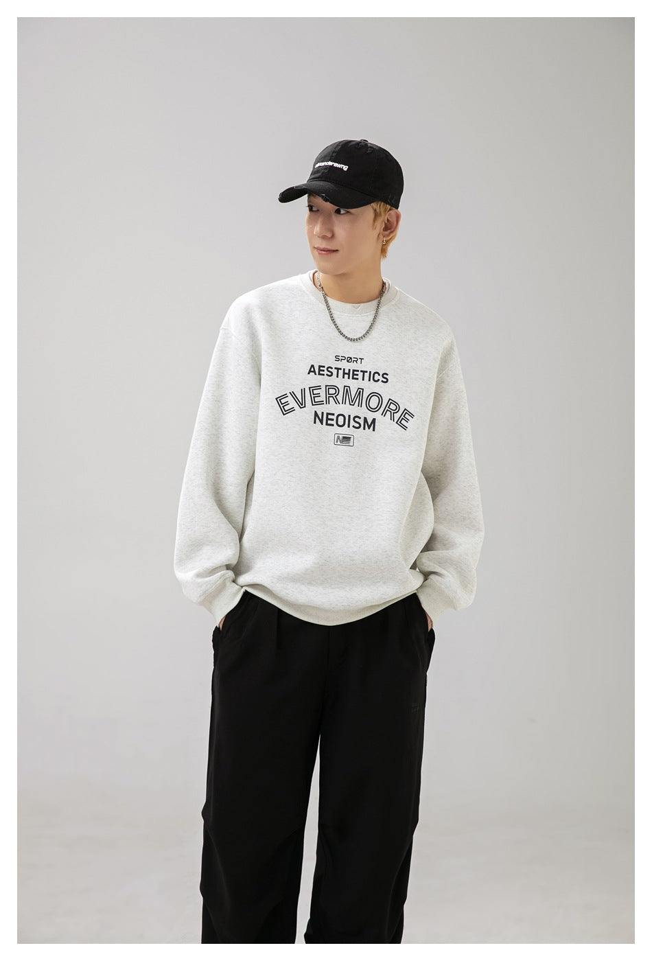 Model wearing a light gray crewneck sweatshirt with dark chest lettering and black pants.
