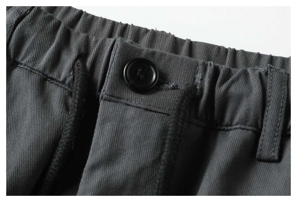 Close-up of the charcoal pants' elastic waistband, black button, drawstring, and belt loop.