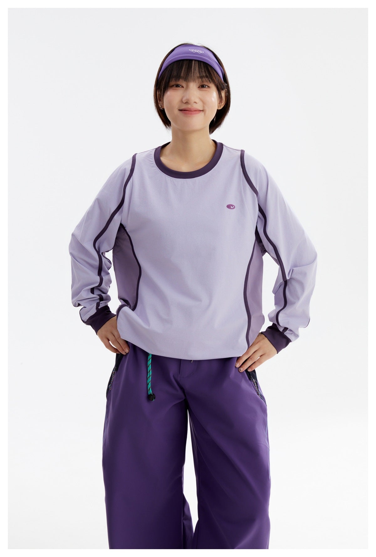Model wearing a light lavender long-sleeve top with dark purple trim and purple trousers, shown from the front.