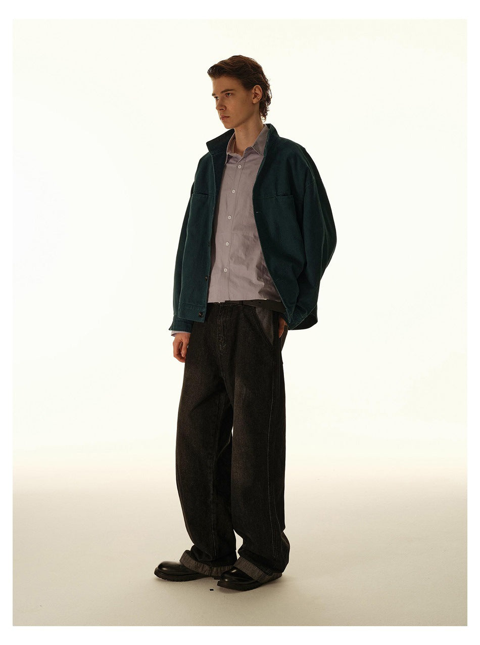 Model in an open dark teal jacket over a lavender shirt and wide-leg dark jeans, side view