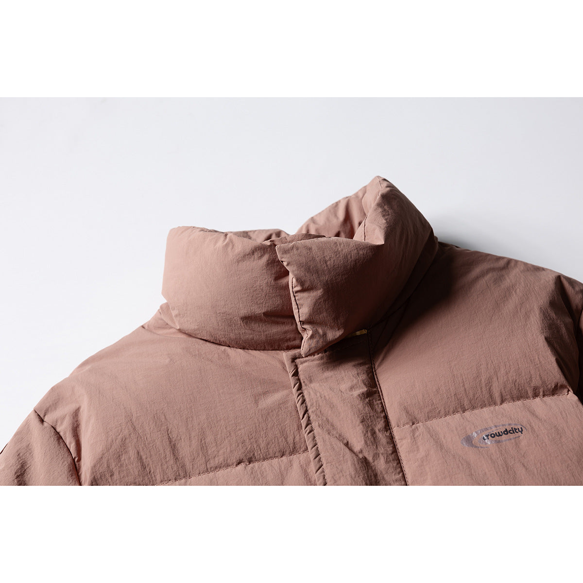 Close-up of the dusty rose puffer jacket's high collar, front placket and small chest logo.
