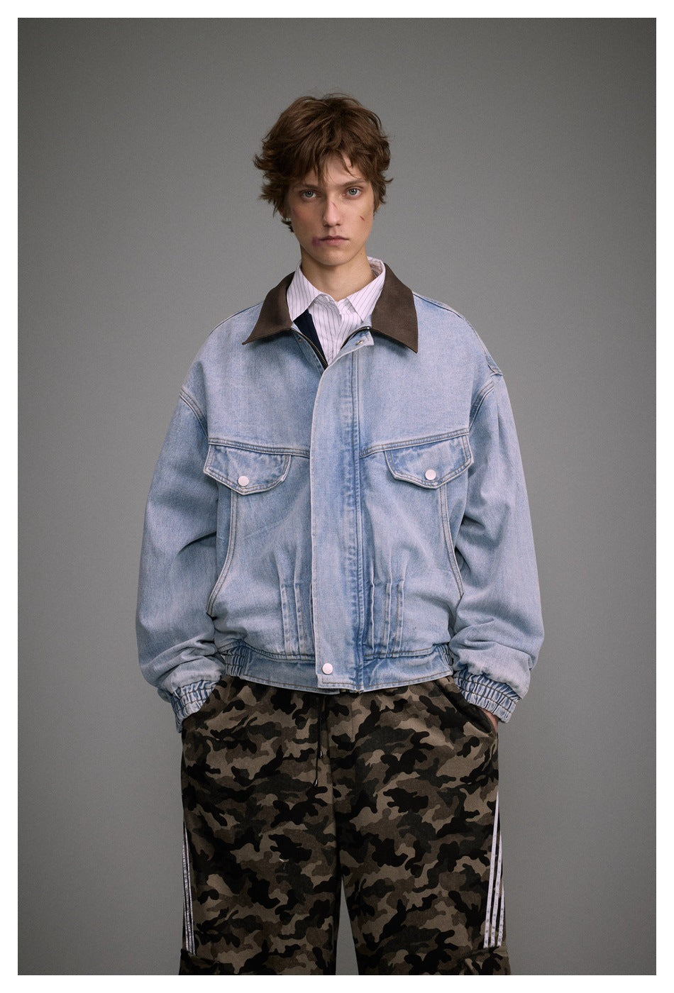 Model wearing a light blue denim jacket with brown collar over a striped shirt and camouflage pants, front view